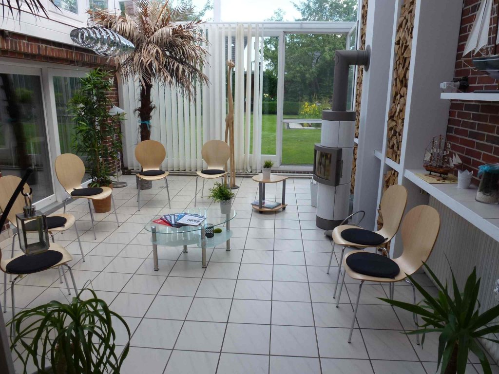 Heller Wartebereich des Salons mit Sitzgruppe, Kaminofen und Blick in den Garten